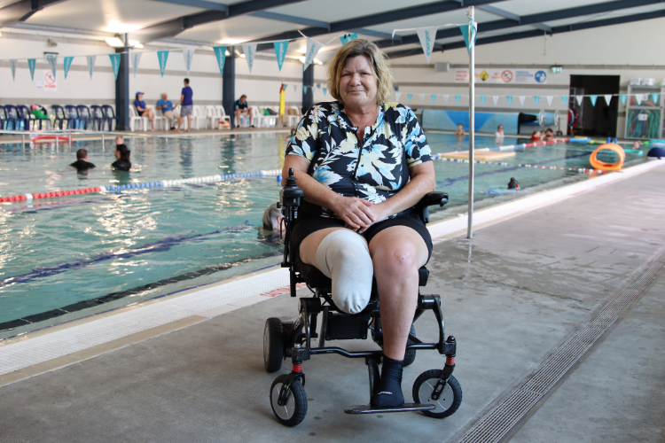 Carol in a wheelchair, smiling and facing forward at the poolside.