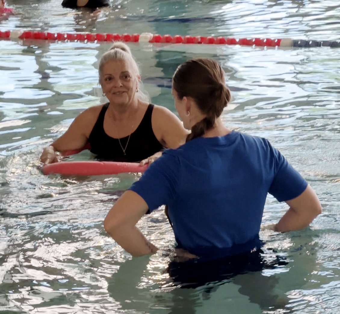 Suzan in the pool holding a pool noodle with her therapist.