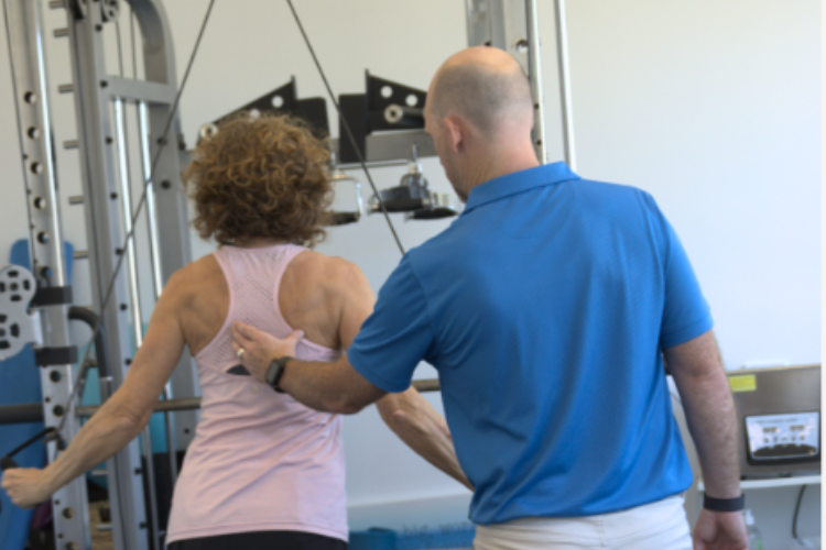 The woman, wearing a light pink tank top, is engaged in a workout while the exercise physiologist, dressed in a blue polo shirt, provides guidance and support at My Health Team.