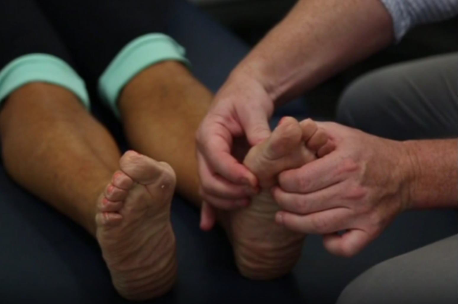 A podiatrist is using a handheld device to assess a patient's feet, focusing on the soles and toes.