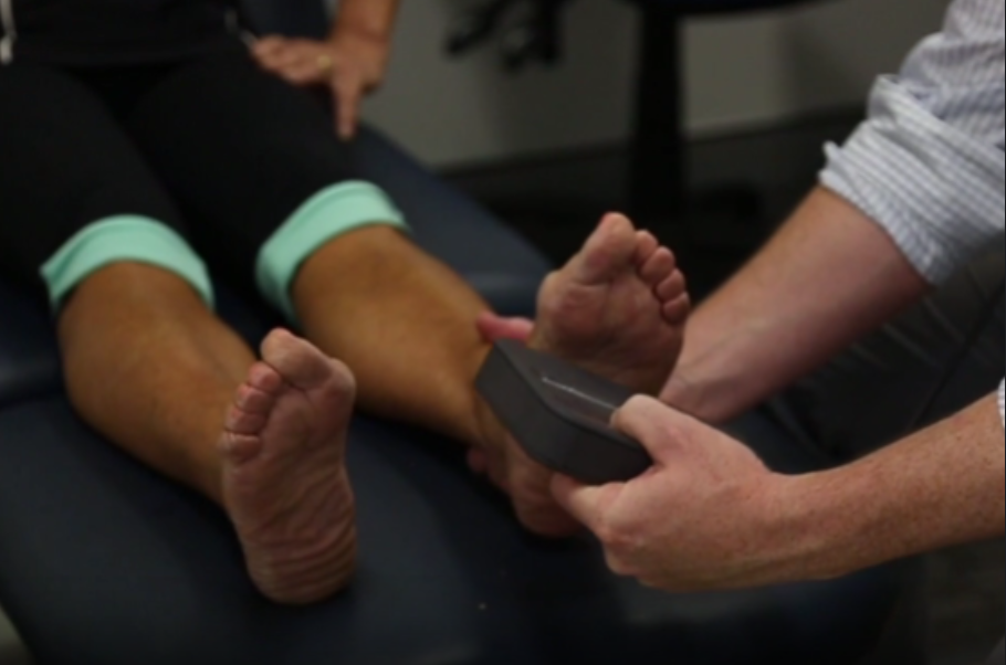 A podiatrist examining a patient's feet, using a diagnostic tool to assess foot alignment and biomechanics. The patient is seated on a medical examination table, with the podiatrist focusing on providing personalised foot care at My Health Team in Redcliffe